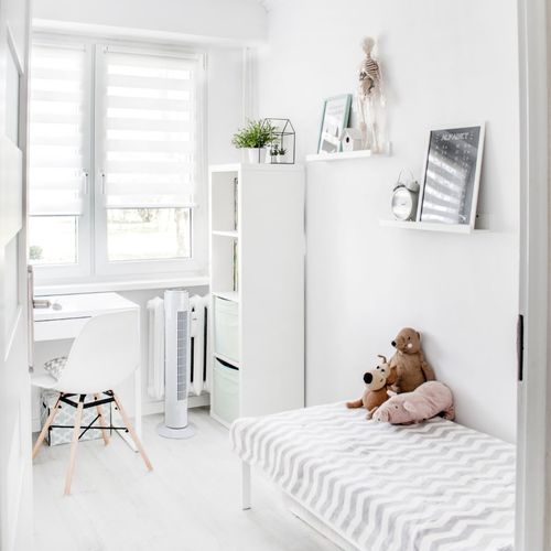 Proche d’un lit et d’un bureau blanc, une pièce moderne et lumineuse avec ventilateur discret près du radiateur. Meilleur ventilateur pour rafraîchir une pièce.