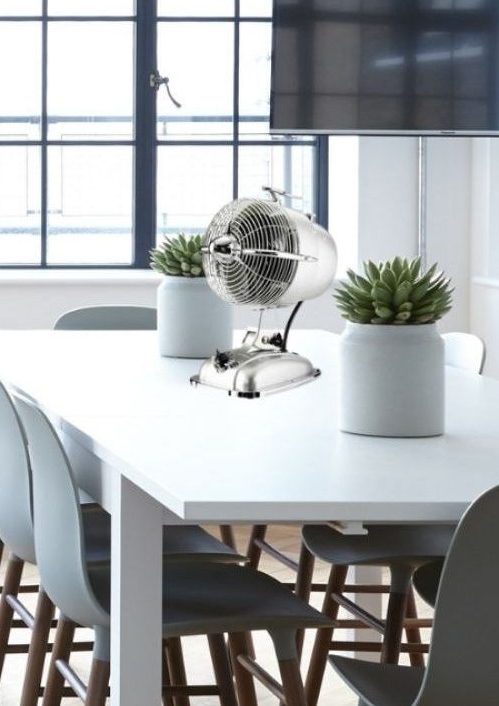 Ventilateur argenté posé sur une table blanche dans une salle lumineuse.