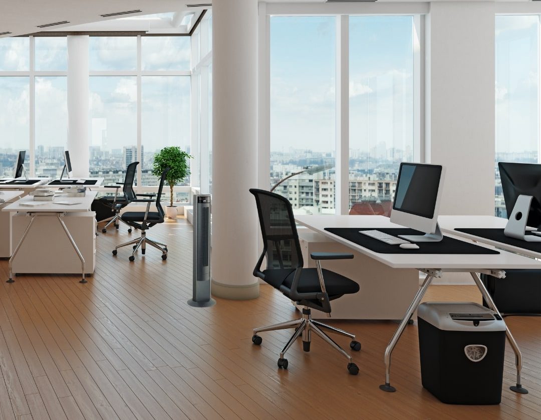 Ventilateur colonne près d’un bureau dans un espace de travail moderne avec plusieurs postes et grande baie vitrée.