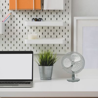 Ventilateur rechargeable gris sur une étagère de bureau près d’un ordinateur portable et d’une plante.